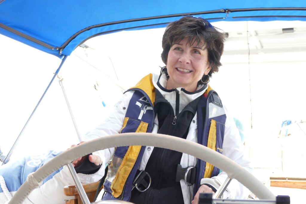 Linda L.M. Worley, MD, author of Smooth Sailing Life, smiling at the wheel of a sailboat