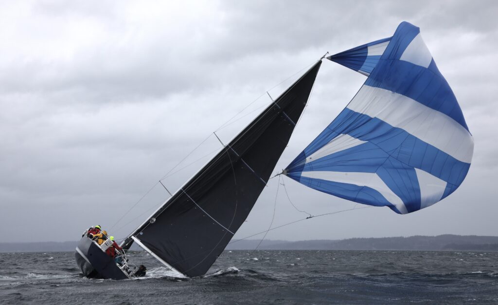 A racing sailboat heeled far over in heavy wind, its spinnaker flying out of control